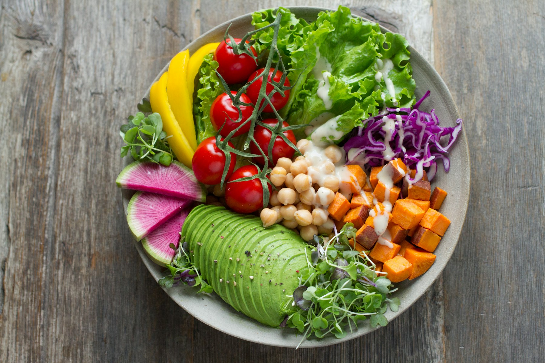 A colorful grain bowl with chickpeas, roasted sweet potato, avocado, tomatoes, and greens